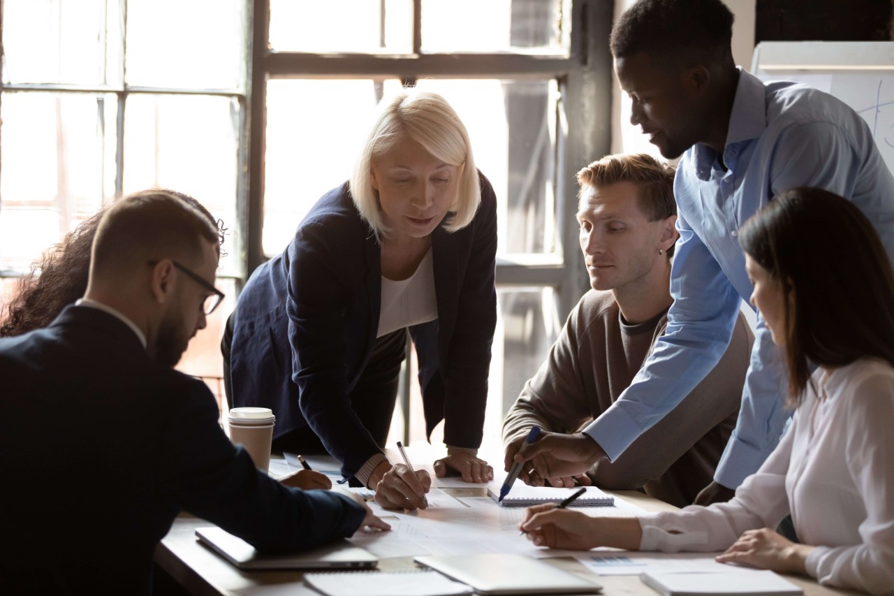 Older leader help diverse team in paperwork analysis at briefing Older leader help diverse team in paperwork analysis at briefing