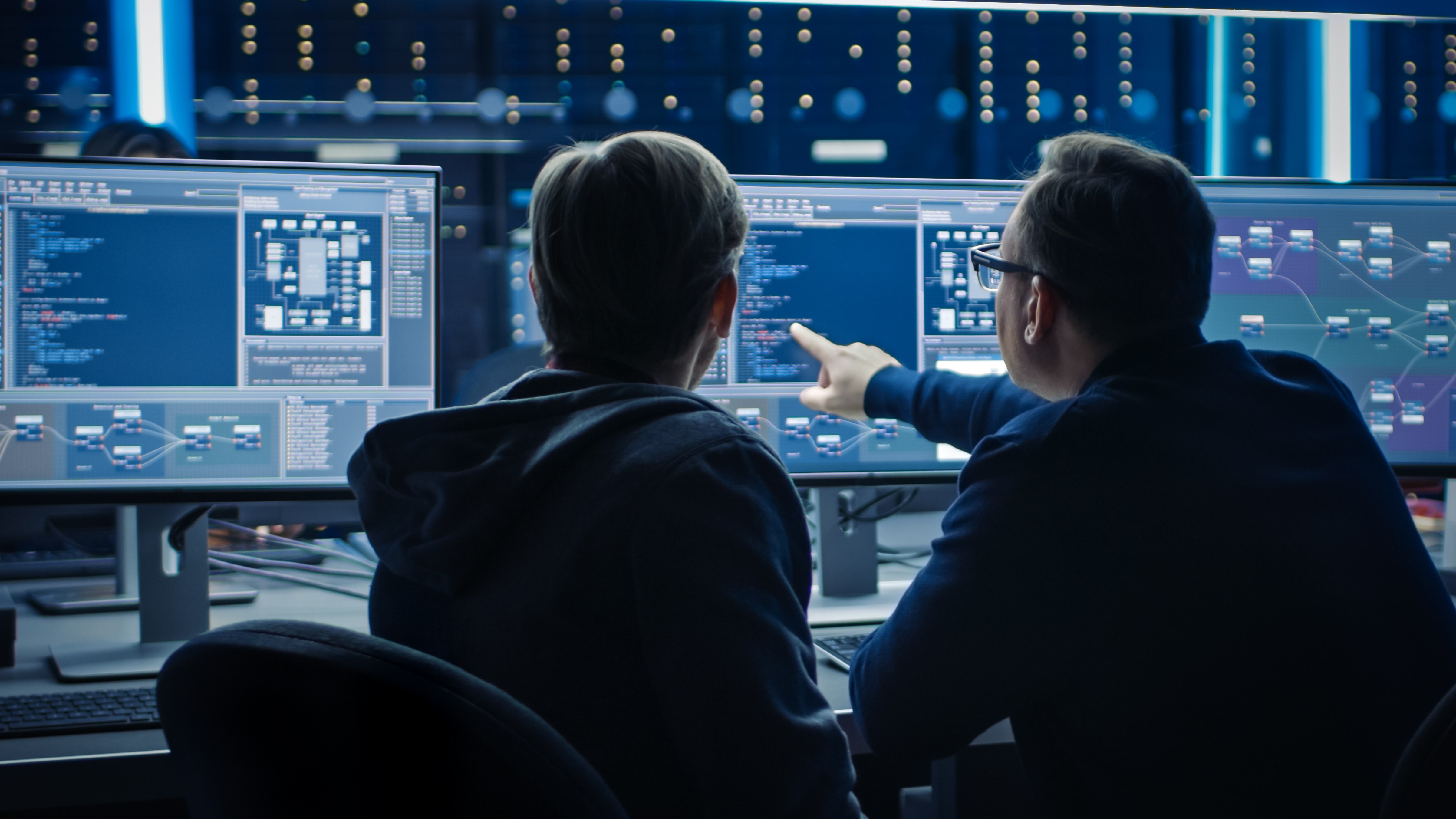 Two Professional IT Programers Discussing Blockchain Data Network Architecture Design and Development Shown on Desktop Computer Display. Working Data Center Technical Department with Server Racks Two Professional IT Programers Discussing Blockchain Data Network Architecture Design and Development Shown on Desktop Computer Display. Working Data Center Technical Department with Server Racks